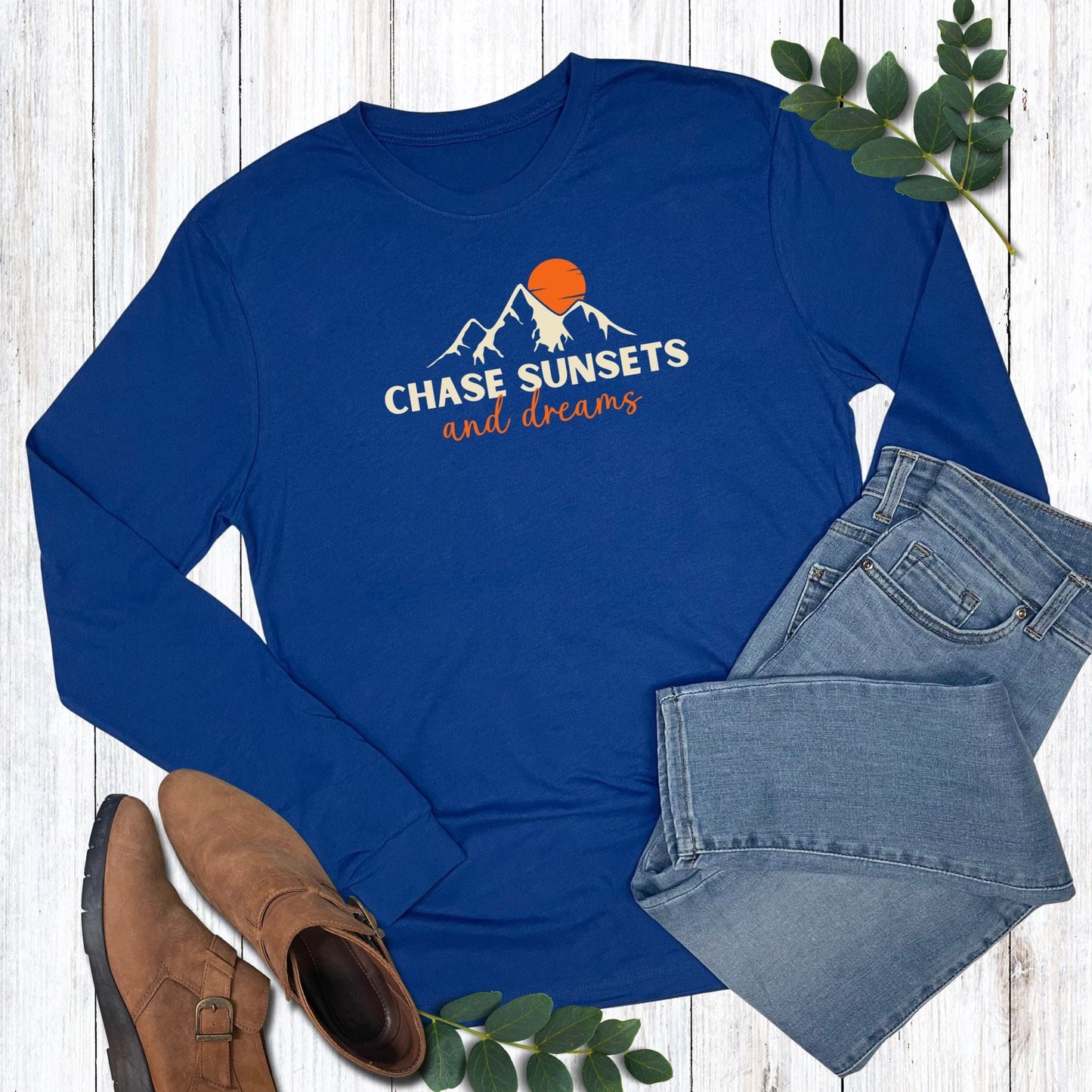 Blue long-sleeve shirt with 'Chase Sunsets and Dreams' text, paired with jeans and boots on a wooden surface.