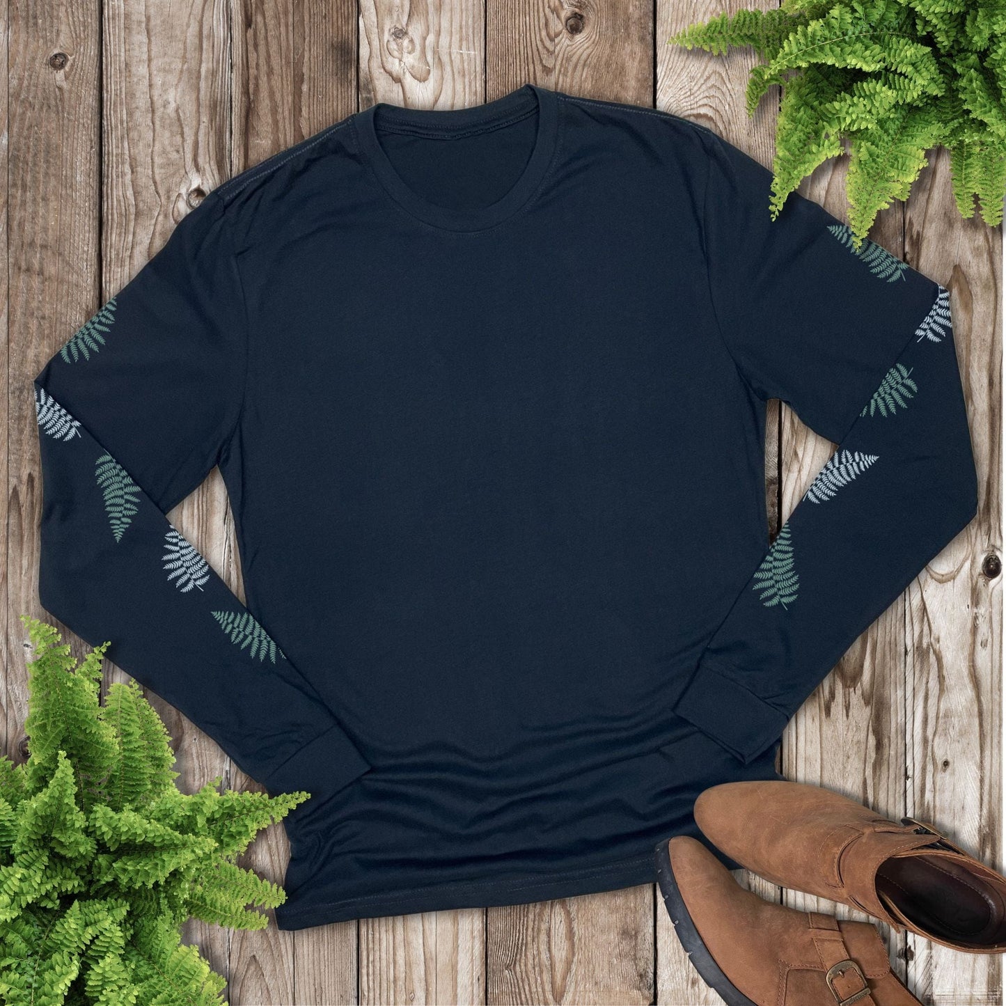 Navy long-sleeve shirt with a fern design down both sleeves, laying on a wooden surface with brown shoes and fern plants.