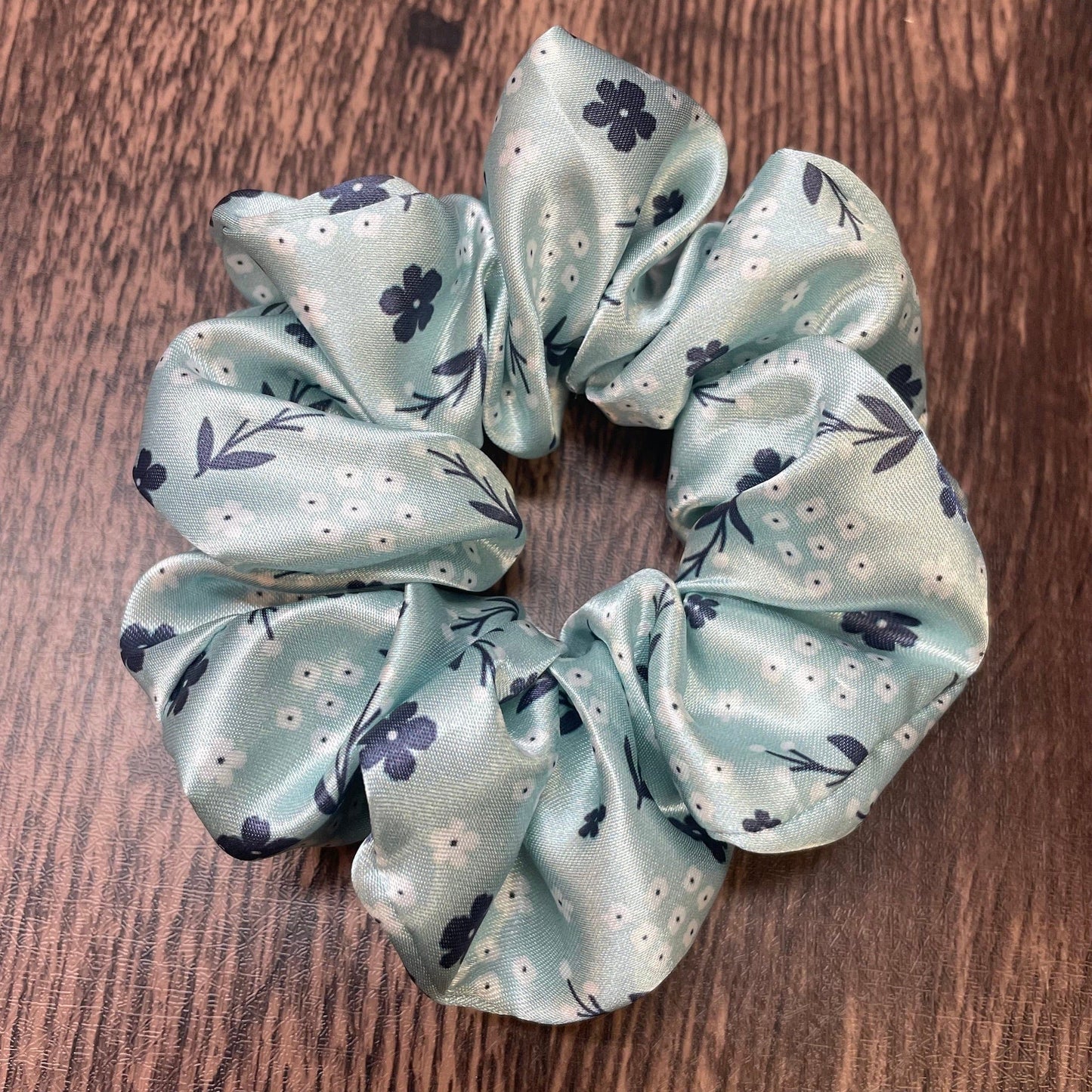 Light green satin scrunchie with floral pattern on a wood background