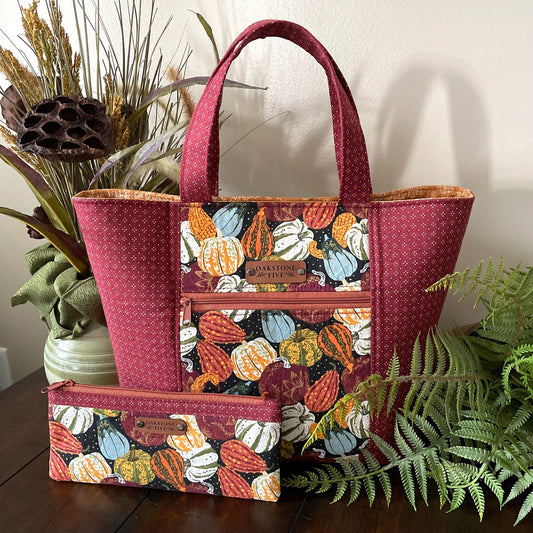 Handmade Autumn tote bag with pumpkin and gourd pattern and matching zipper pouch sitting on a table with plants