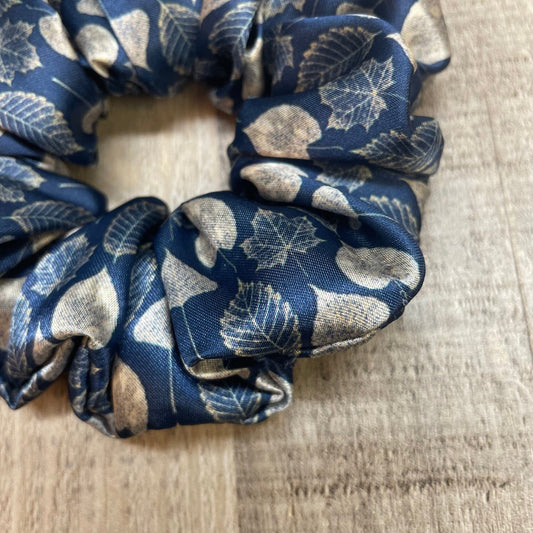 A close-up of a navy blue satin scrunchie with leaf pattern on a wooden background