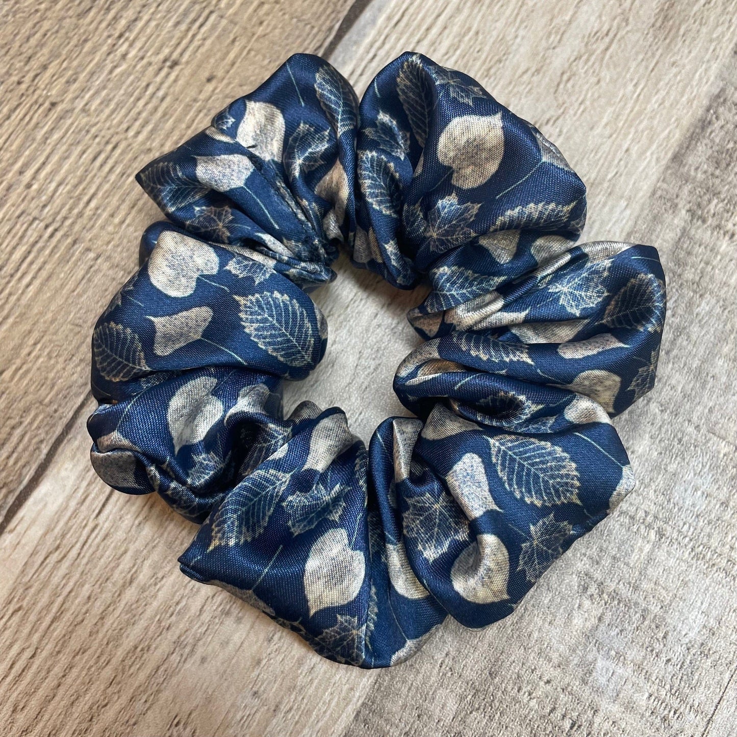 Navy blue satin scrunchie with leaf pattern on a wooden background