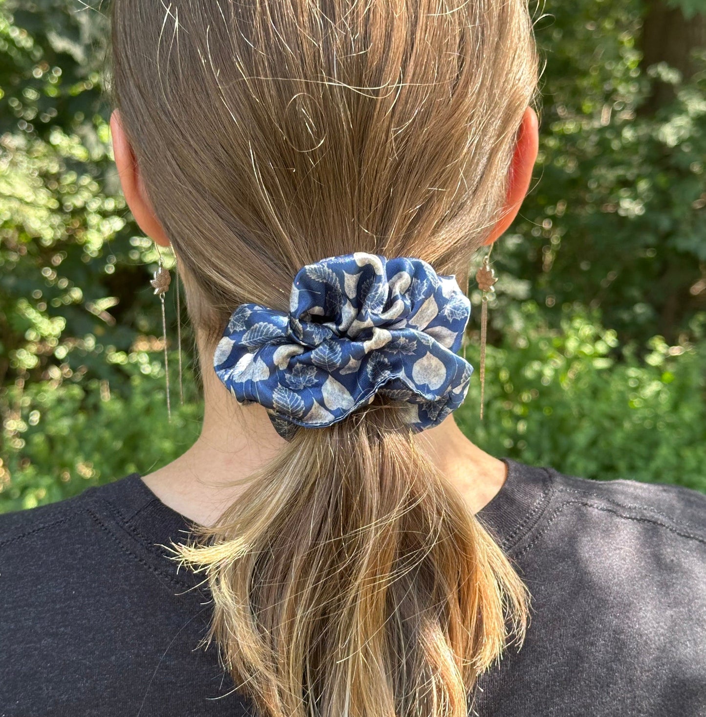 A outdoor photo of a girl wearing a leaf pattern navy satin scrunchie for her ponytail.