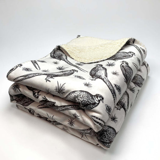 A folded sherpa throw blanket with a pheasant patterned front and a sherpa backing, on a white background