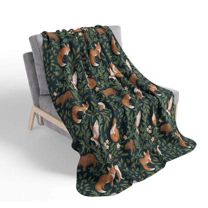 Sherpa blanket with forest-themed pattern featuring bears, foxes, and owls, draped over a chair, on a plain white background