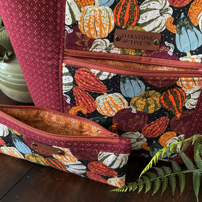 Close-up of a beautiful, handmade seasonal tote bag with pumpkin and gourd fall pattern and matching zipper pouch, siting on a table with a fern.