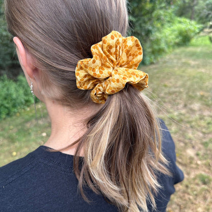 A photo of a woman standing outside wearing a yellow honeycomb patterned scrunchie in her hair.