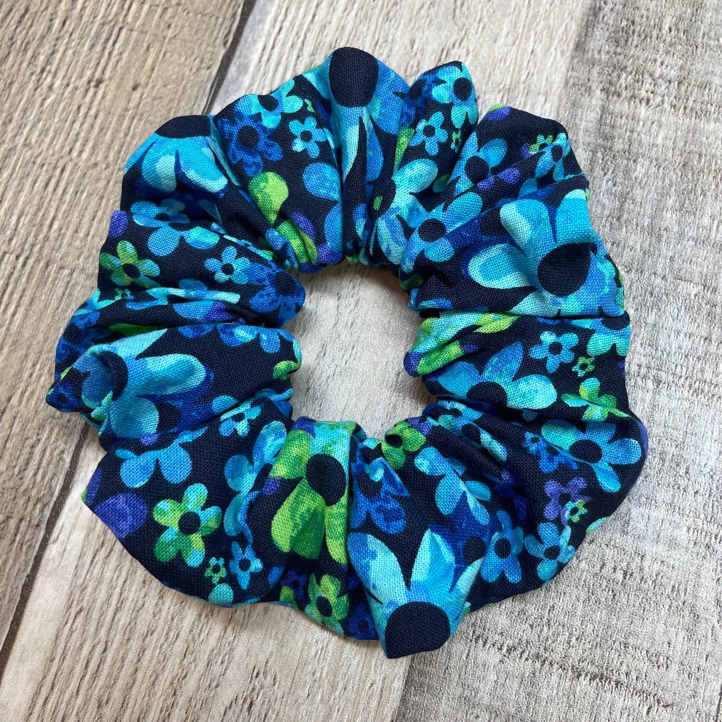 A cute, blue and green daisy floral scrunchie laying on a wooden table