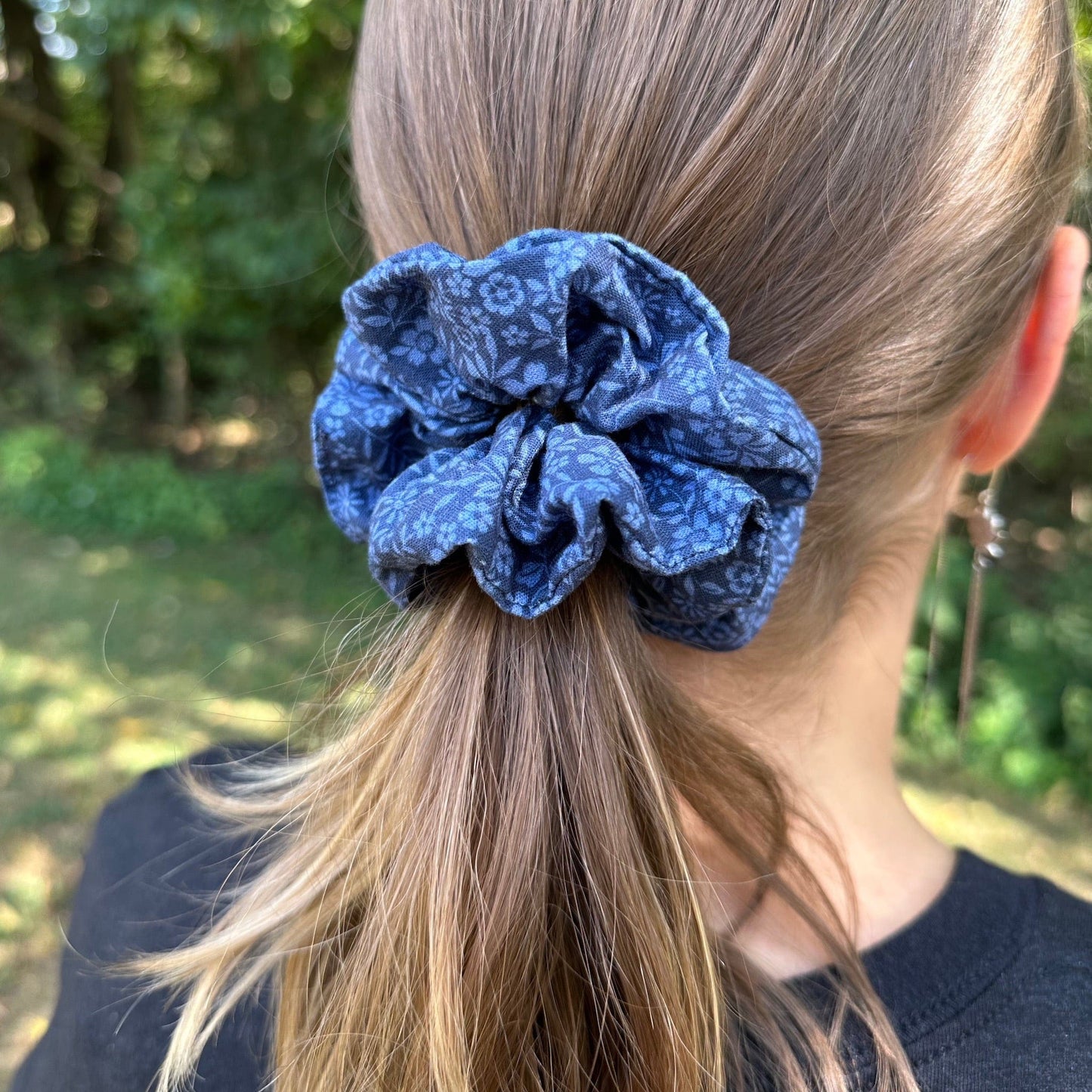 A girl standing outdoors wearing a blue floral cotton scrunchie in her hair.