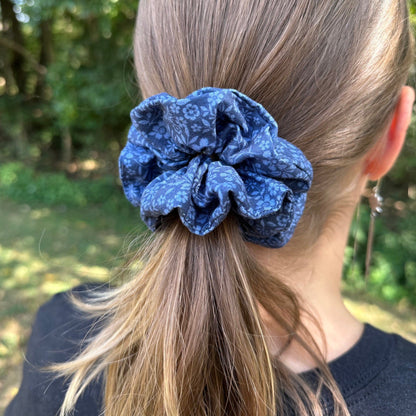 A girl standing outdoors wearing a blue floral cotton scrunchie in her hair.
