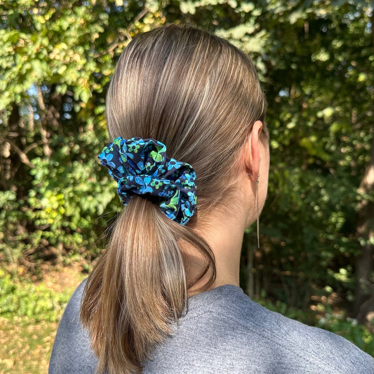 A woman standing outside with a blue daisy floral scrunchie in her hair.