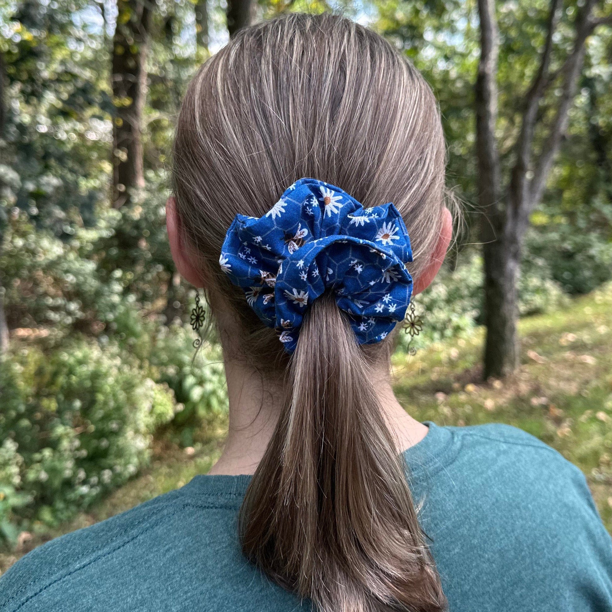 Woman standing outsider with a blue honey bee and flowers hair scrunchie in her ponytail.