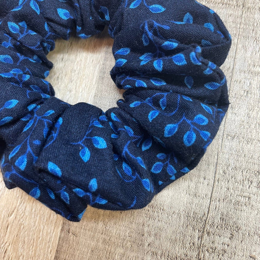 Close up of a navy blue scrunchie with blue leaf and vines pattern on a wooden background