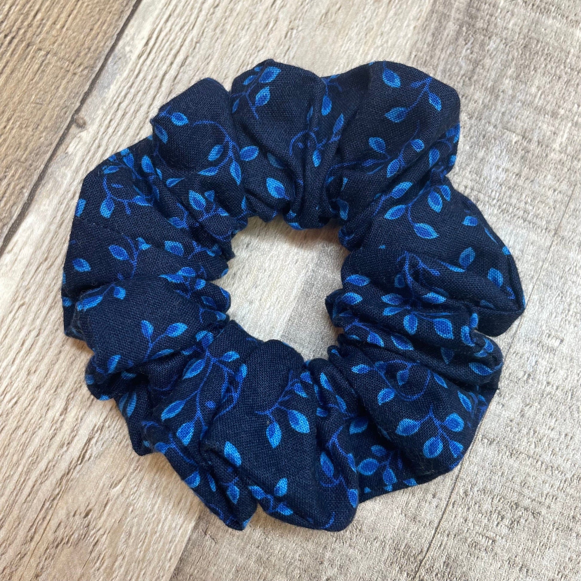 Navy blue scrunchie with blue leaf and vines pattern on a wooden background