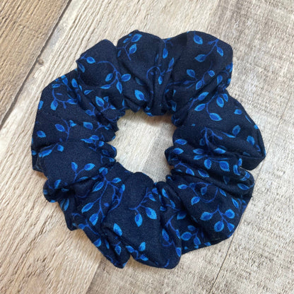 Navy blue scrunchie with blue leaf and vines pattern on a wooden background
