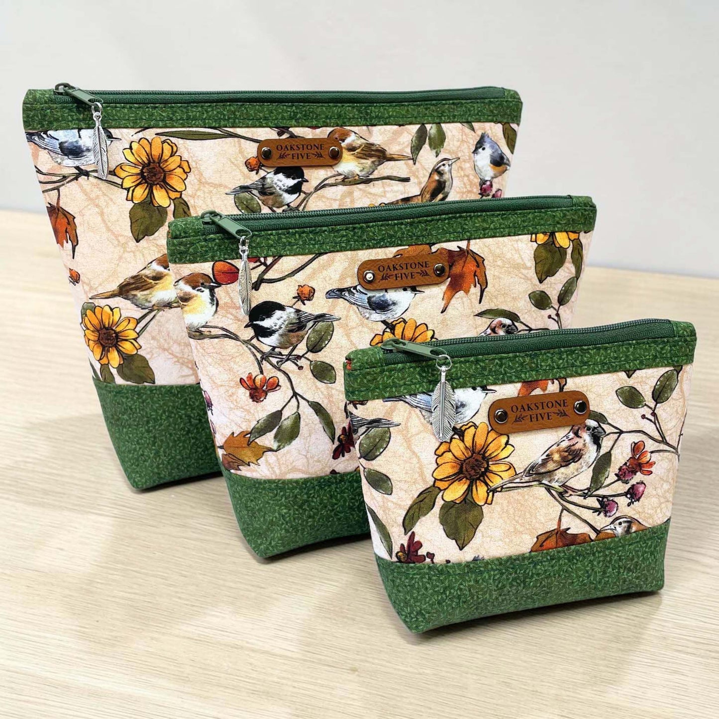 Three handmade zipper pouches with bird design, on a light wooden surface.