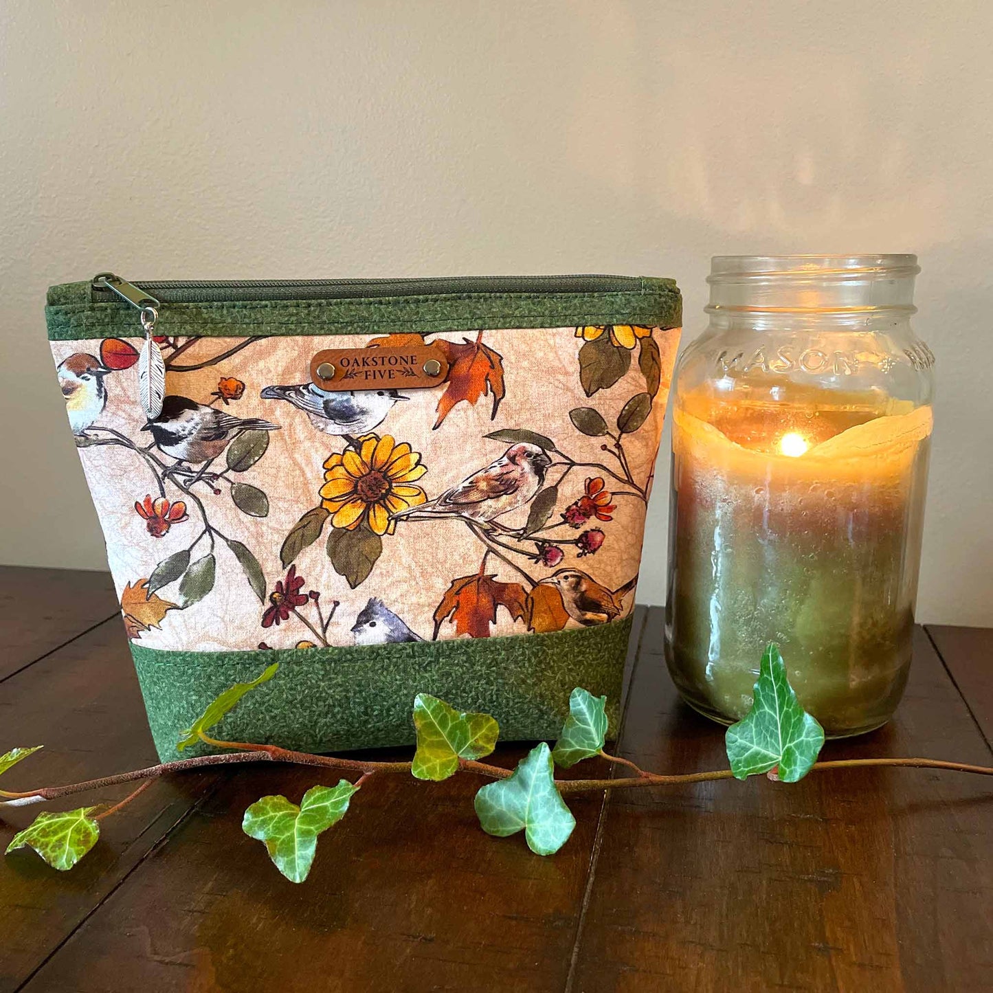 Medium size zipper pouch with flower and bird pattern, sitting next to a lit candle on a wooden surface with some ivy