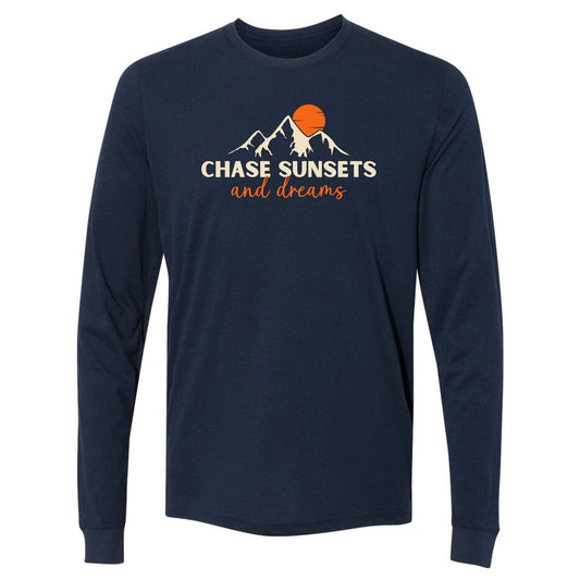 A navy, long-sleeve chasing sunsets shirt for nature lovers. Has an image of a mountain range and sun and says, "Chase Sunsets and Dreams."
