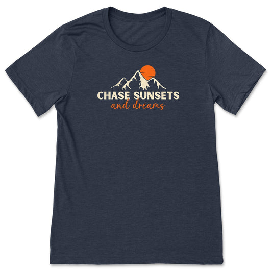 A navy nature t-shirt that has mountains with an orange sunset and says, "Chase Sunsets and Dreams."