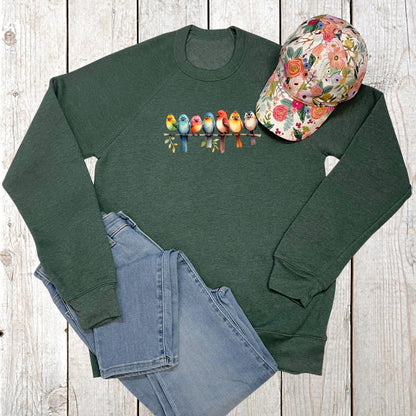 Green sweatshirt with colorful bird design, floral cap, and blue jeans on a wooden surface
