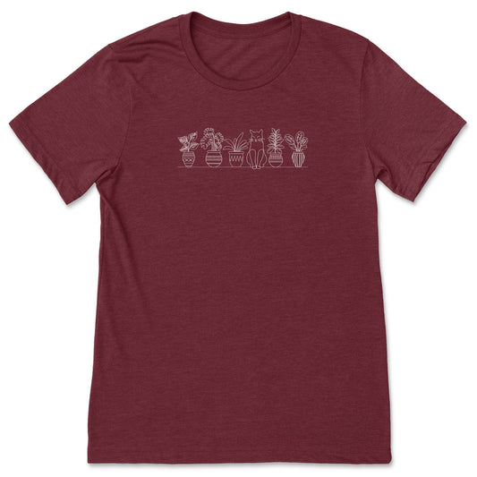 A cute, deep red, plant t-shirt that has a simple line art drawing of potted plants on a shelf with a cat sitting between them - a great gift for plant lovers and gardeners!