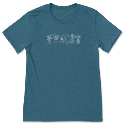 A cute, teal, plant t-shirt that has a simple line art drawing of potted plants on a shelf with a cat sitting between them - a great gift for plant lovers and gardeners!