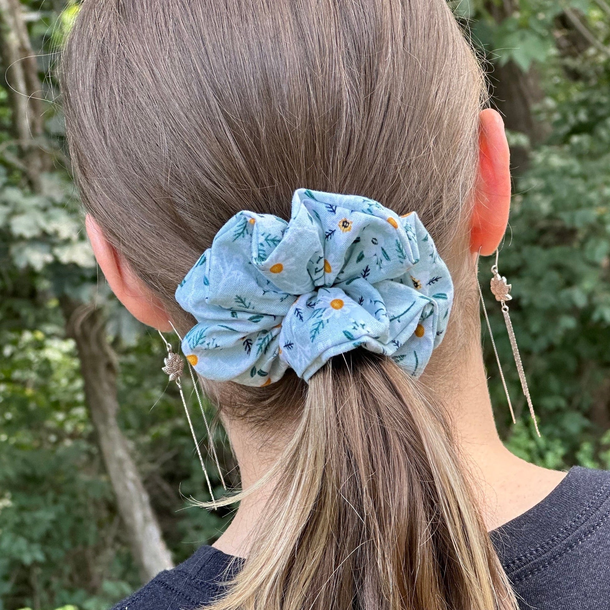 A woman wearing a light green floral scrunchie in her ponytail.