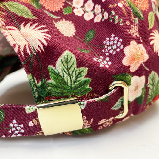 Close-up of gold metal hardware on women's floral baseball cap with dahlia flower pattern.