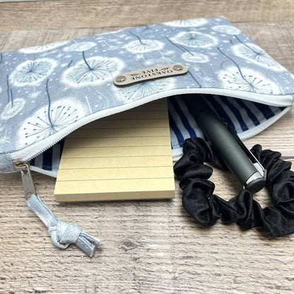 Fabric dandelion zipper pouch with stationery items on a wooden surface