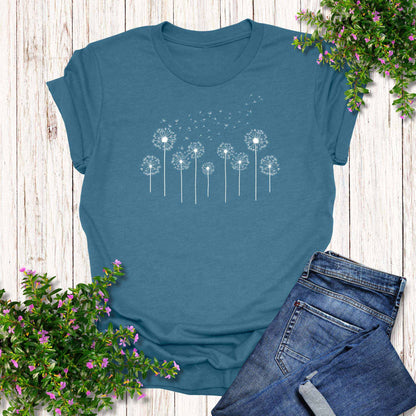 Teal t-shirt with dandelion design on a wooden surface with jeans and flowers.