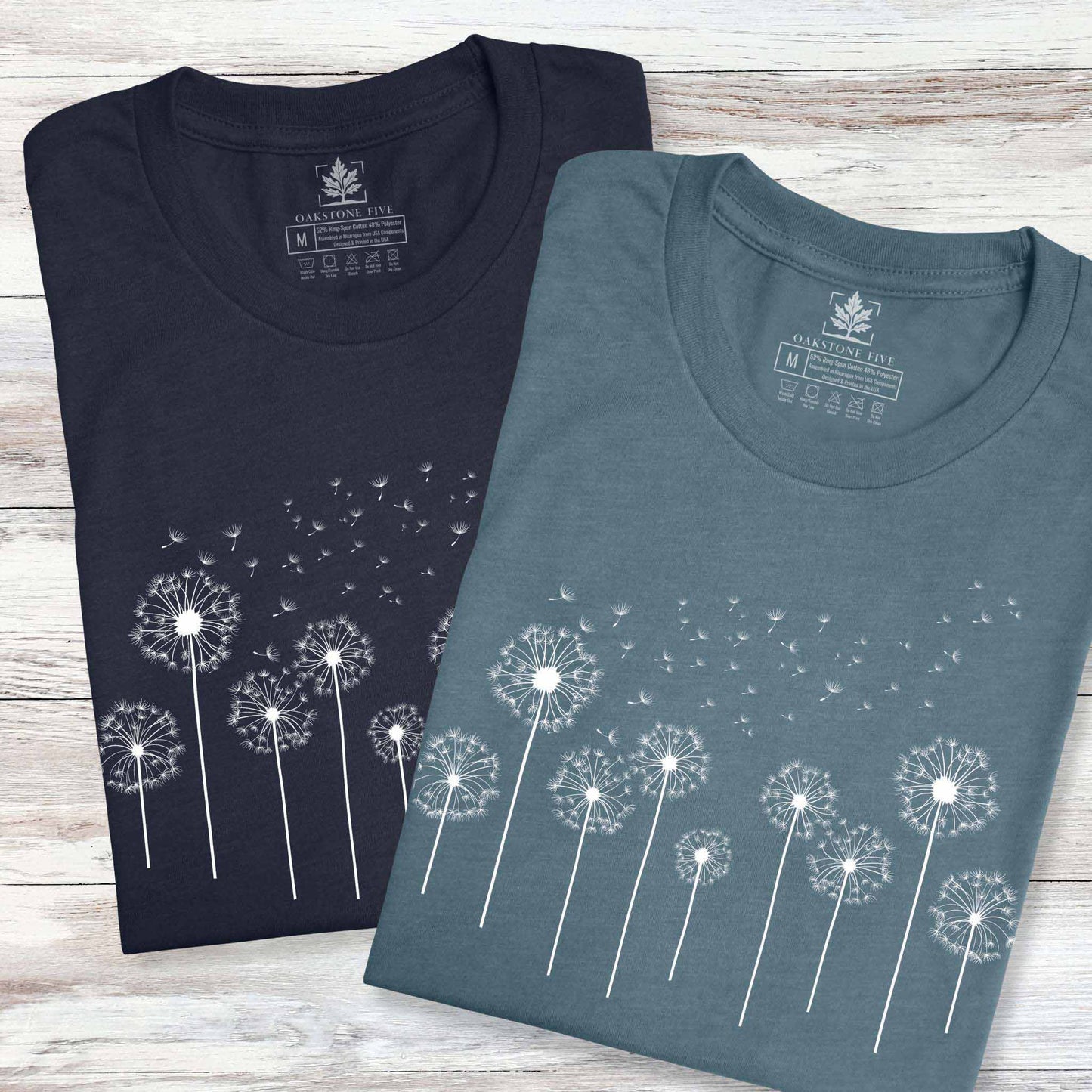 Two folded t-shirts with dandelion design on a wooden surface