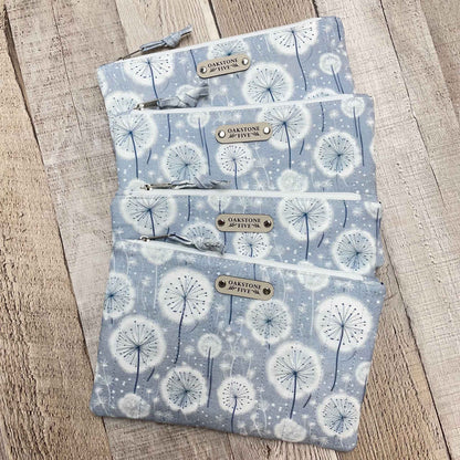 4 zipper pouches with dandelion pattern on a wooden surface