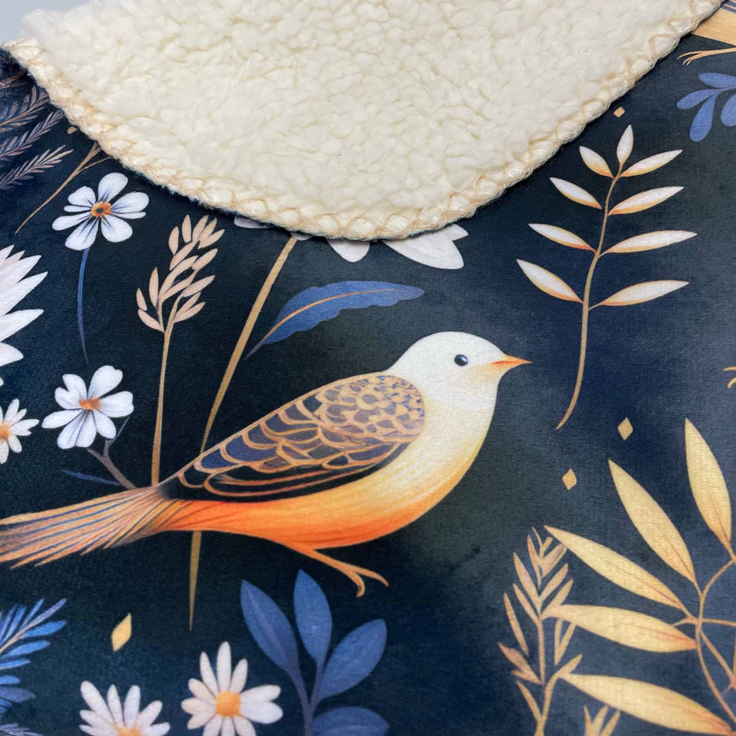 A close-up of a nature-inspired sherpa blanket featuring a dark background with a bird and botanical motif