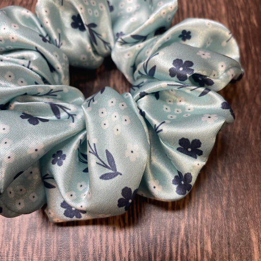 Close-up of a light green satin scrunchie with floral pattern on a wood background