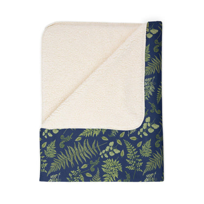 A folded sherpa blanket with a fern and leaf pattern with a blue background