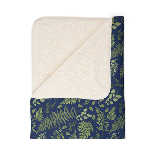 A folded sherpa blanket with a fern and leaf pattern with a blue background