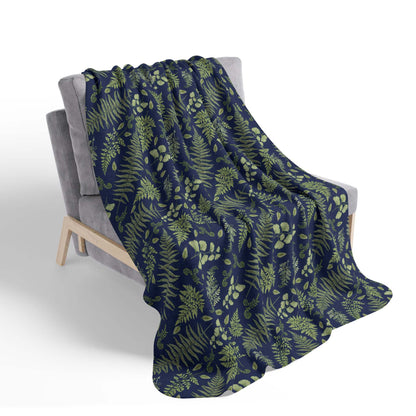 A nature-inspired sherpa throw blanket with a fern and leaf pattern, laying over a chair, on a white background