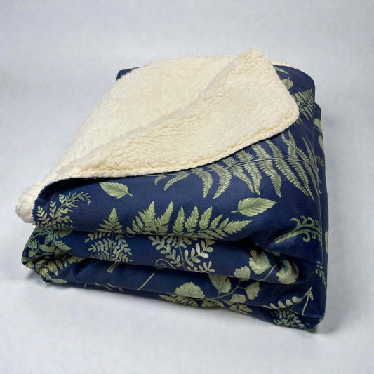 A folded sherpa blanket with a nature-inspired fern and leaf pattern with a dark blue background