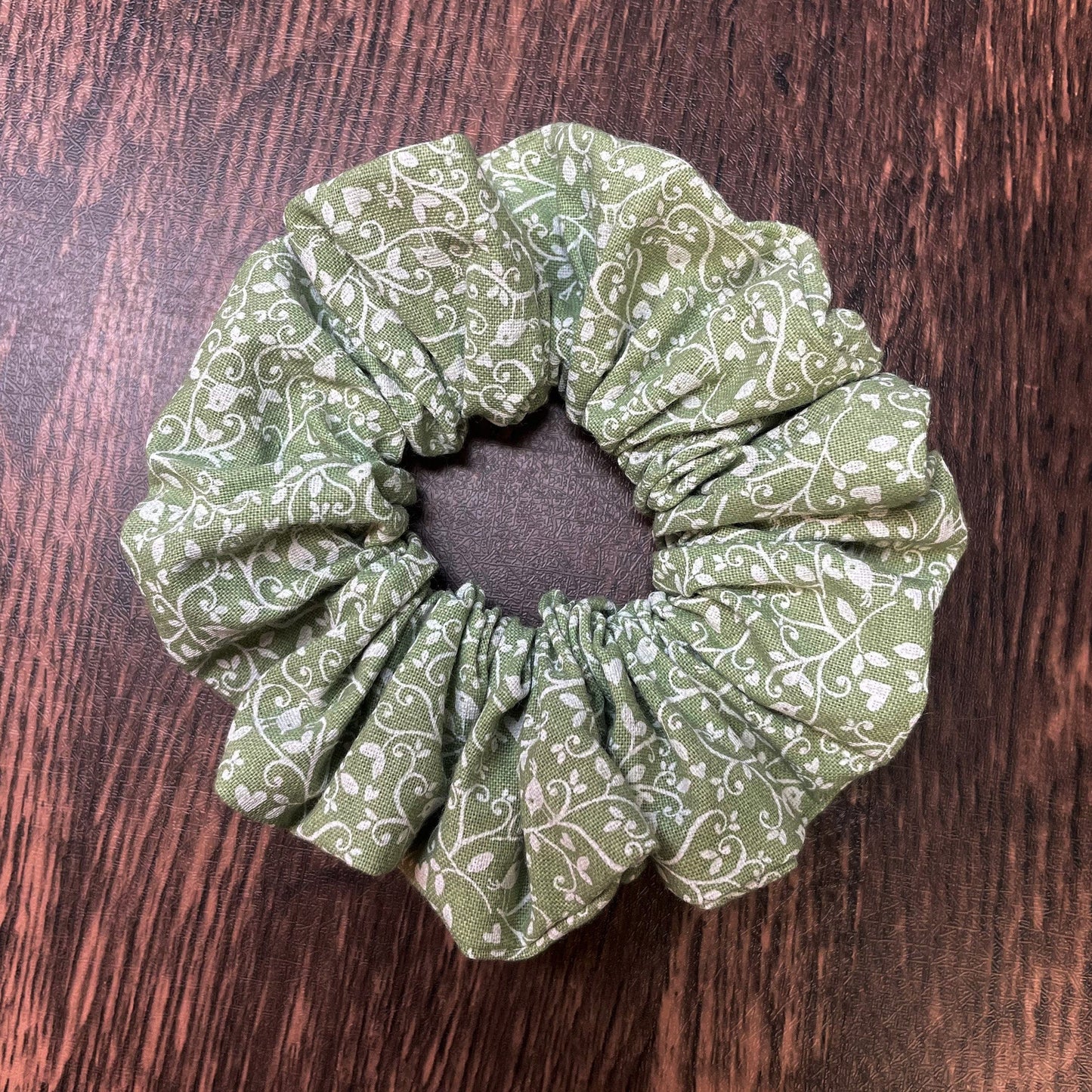 Green scrunchie with white floral and bird pattern on a wood background