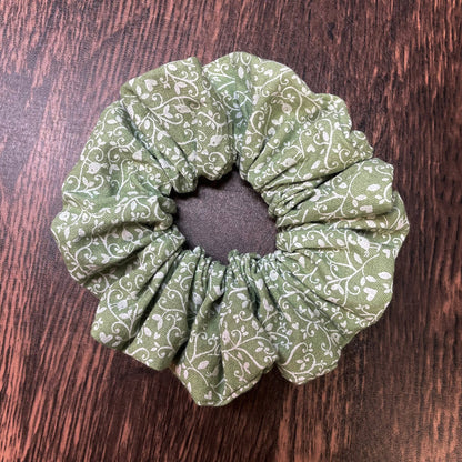 Green scrunchie with white floral and bird pattern on a wood background