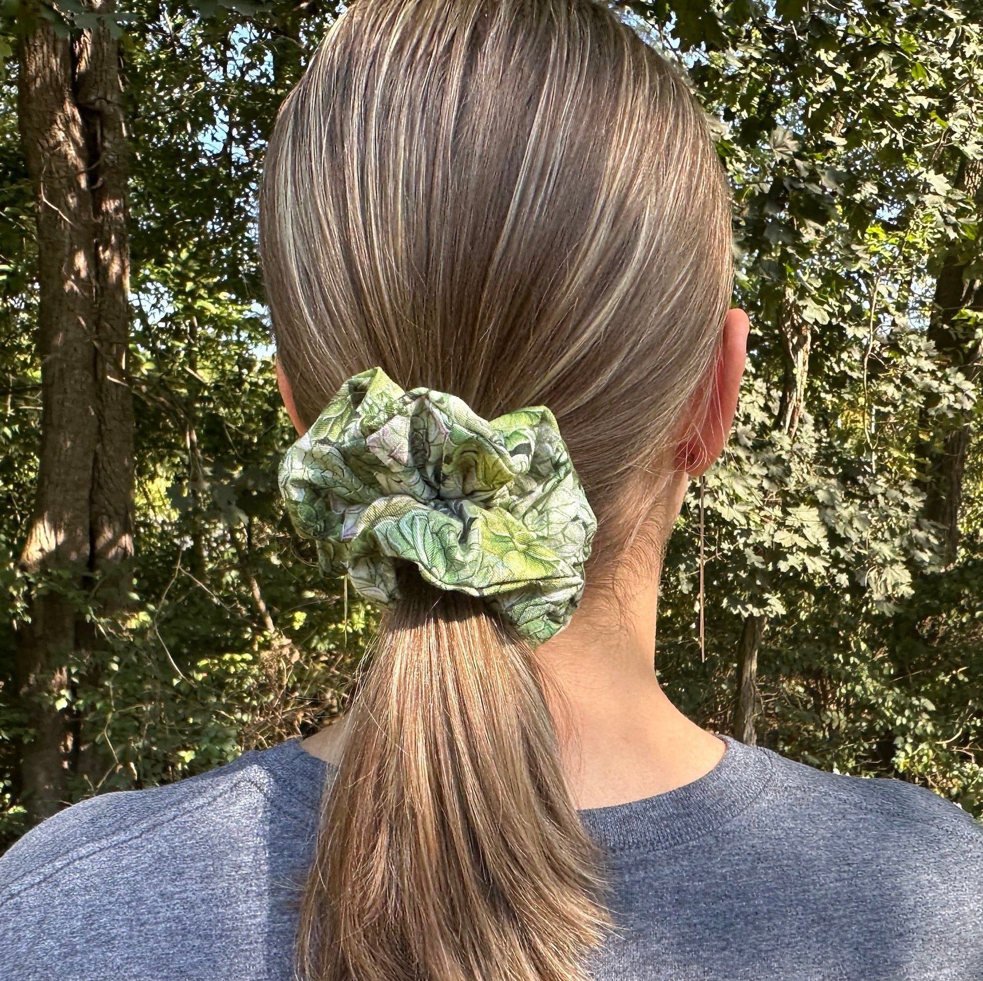 Girl standing in the woods wearing a green succulent scrunchie in her hair