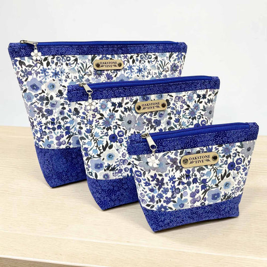 Three floral-patterned pouches with blue accents on a wooden surface.