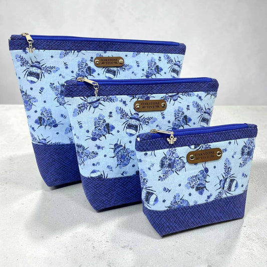 Set of three blue floral bumble bee patterned zipper pouches on a light gray background