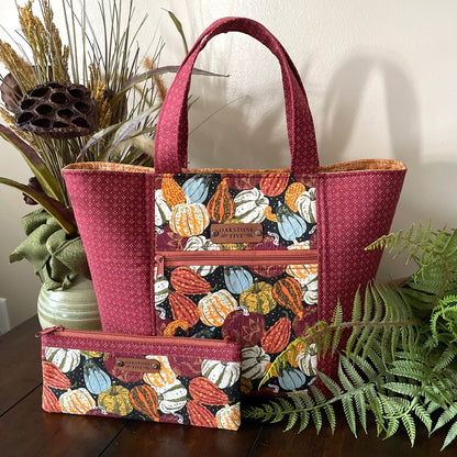 Handmade Autumn tote bag with pumpkin and gourd pattern and matching zipper pouch  sitting on a table with plants