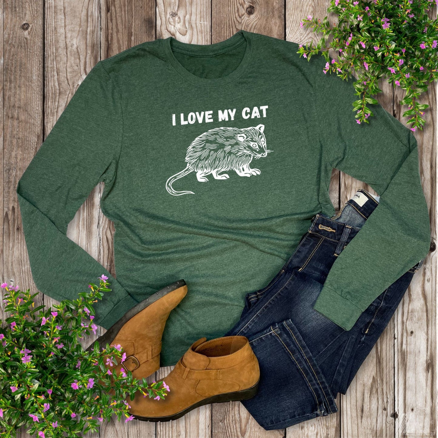 Green long-sleeve shirt with 'I Love My Cat' graphic, paired with jeans and boots on a wooden surface with flowers.