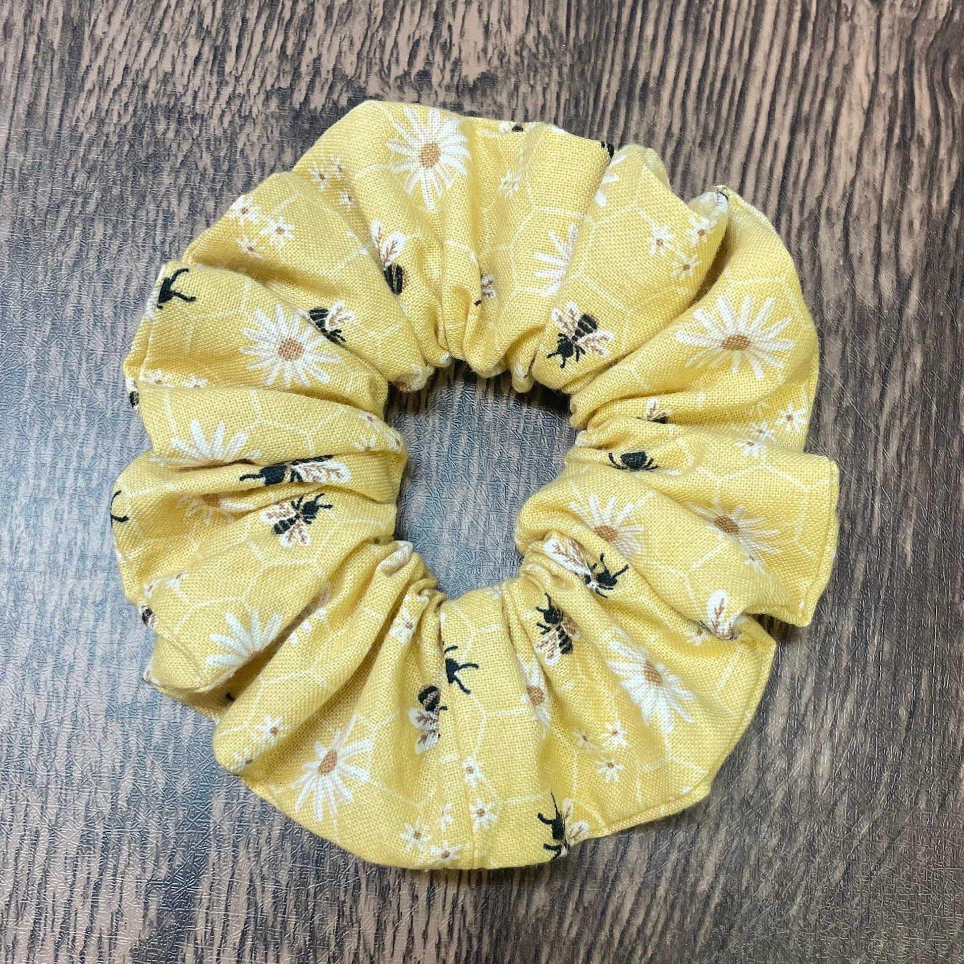 Yellow scrunchie with honey bee and floral pattern on a wood background