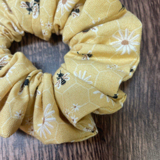 Close-up of a yellow scrunchie with honey bee and floral pattern on a wood background