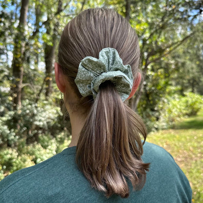 Woman standing outdoors wearing her hair up in a ponytail with a light green bird and floral design.