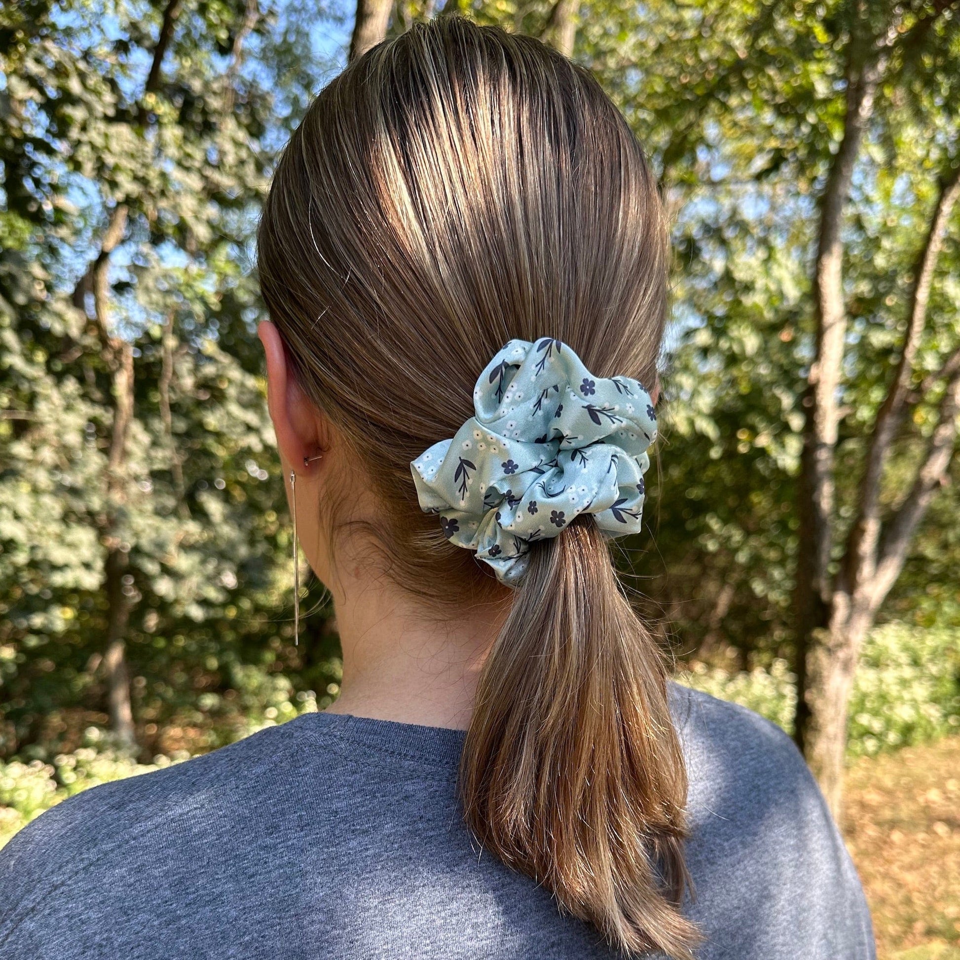 Women wearing her hair in a ponytail with a light green, satin, floral scrunchie