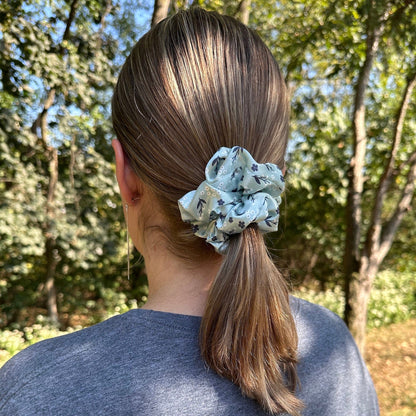 Women wearing her hair in a ponytail with a light green, satin, floral scrunchie